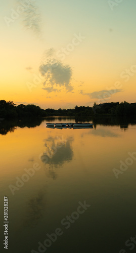 tranquil, twilight sunset shot over lake with reflections of sky and clouds in water and rowing boats to centre of lake