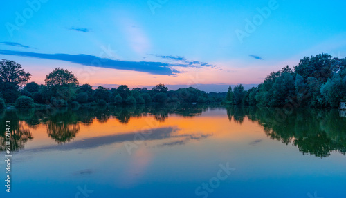 tranquil, twilight sunset shot over lake with reflections of sky and clouds in water and rowing boats to centre of lake