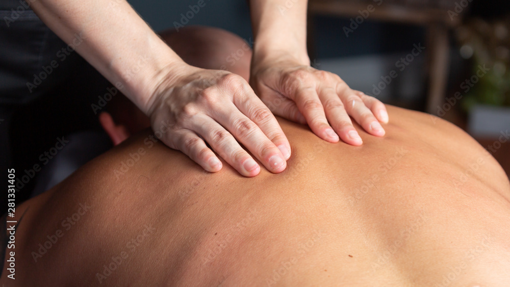 The hands of a massage therapist work on the muscles in a man's back. The hands of a massage therapist work on the muscles in a man's back.