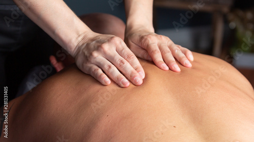 The hands of a massage therapist work on the muscles in a man's back.