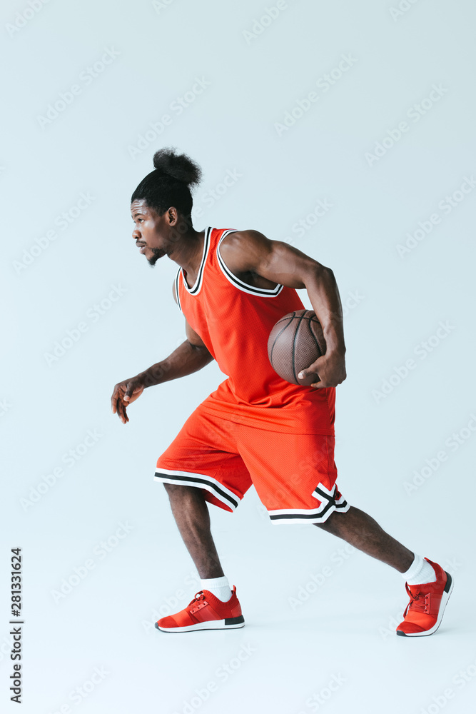 african american sportsman in red sportswear playing basketball on grey background