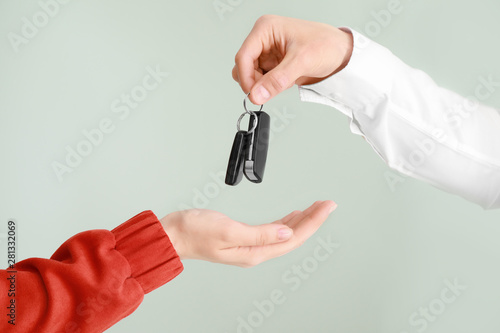 Salesman giving car keys to woman on light background