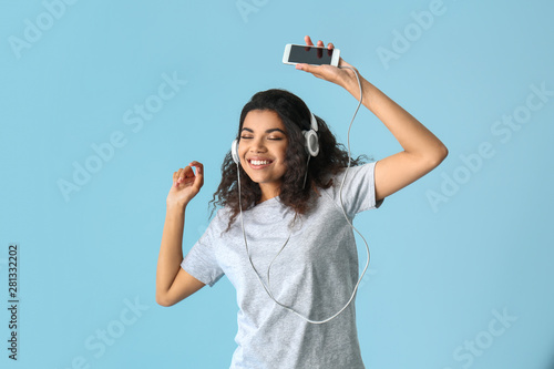 Portrait of happy African-American woman listening to music on color background