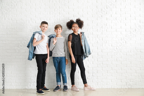 Stylish children in jeans clothes near white brick wall