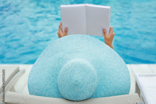 Obraz na plátně Beautiful young woman reading book while relaxing on sun lounger near swimming p