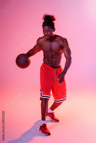 shirtless african american sportsman in red shorts playing basketball on pink background with gradient and lighting