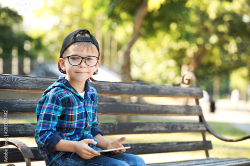 Cute little boy with tablet computer sitting on bench in park