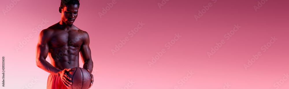 panoramic shot of shirtless, muscular african american basketball player holding ball on dark pink background with gradient