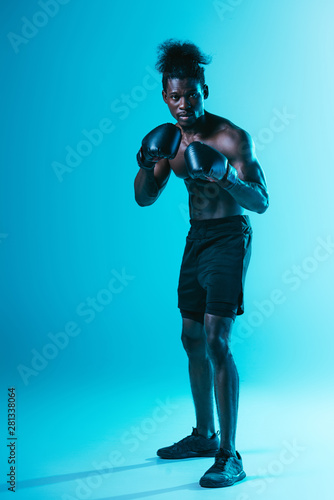 shirtless african american boxer with muscular torso looking at camera on blue background
