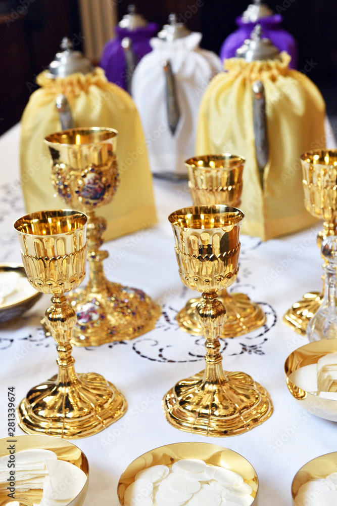 Golden chalices on the altar on top of a white table top.