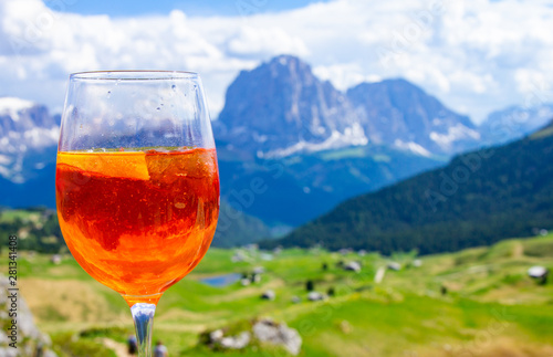 View of the traditional Italian alcoholic drink Aperol Spritz on the background of colorful Italian meadows and the Dolomites Alps mountains. village St. Cristina di Val Gardena Bolzano Seceda, Italy.