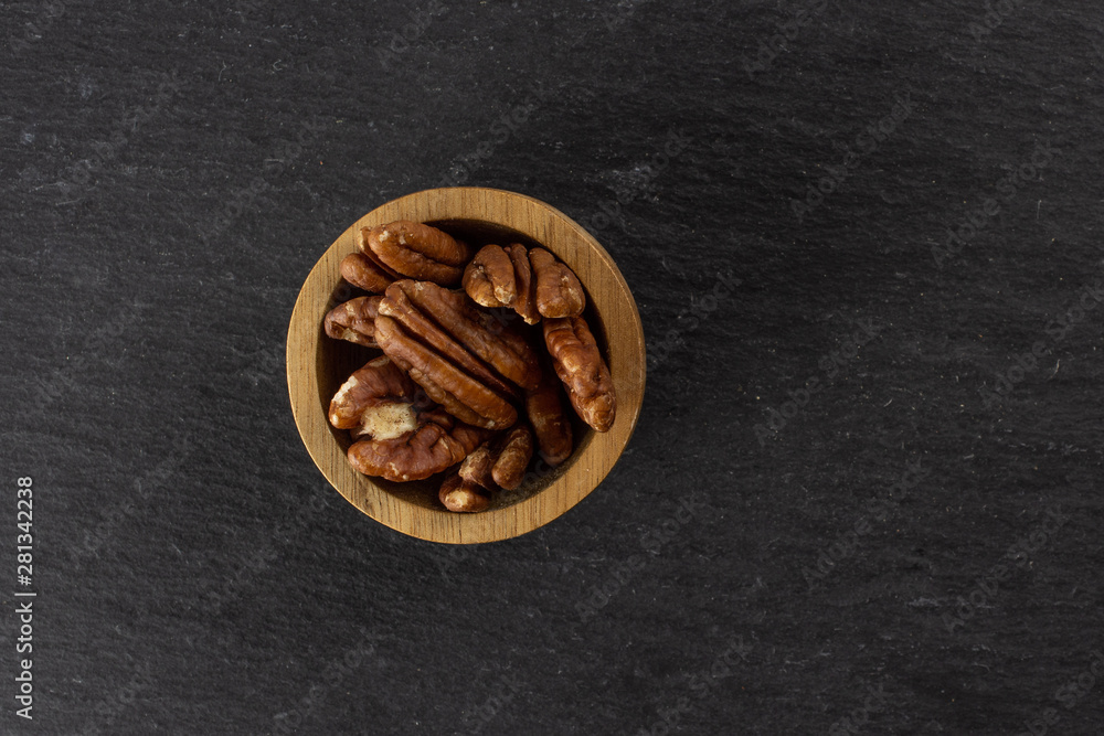 Lot of whole fresh brown pecan nut half copyspace on right in a wooden bowl flatlay on grey stone Lot of whole fresh brown pecan nut half copyspace on right in a wooden bowl flatlay on grey stone