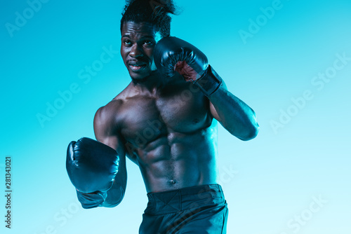 handsome, muscular african american sportsman boxing on blue background