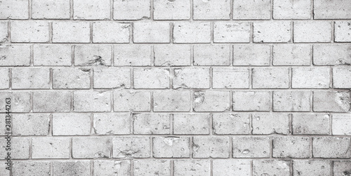 Simple grungy grey white brick wall pattern surface texture wide panorama banner background. Wall weathered under the elements and marked with holes, cracks and imperfections.