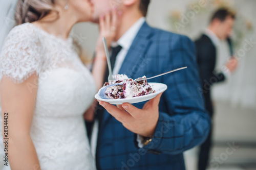 Canvas Print The bride and groom kiss and hold on hand with a plate a delicious wedding cake
