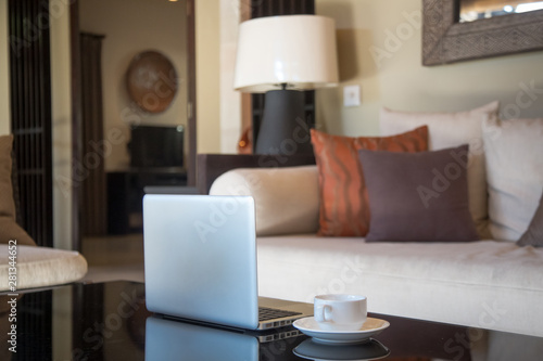 Laptop and a cup of coffee on the coffee table in a modern cozy living room
