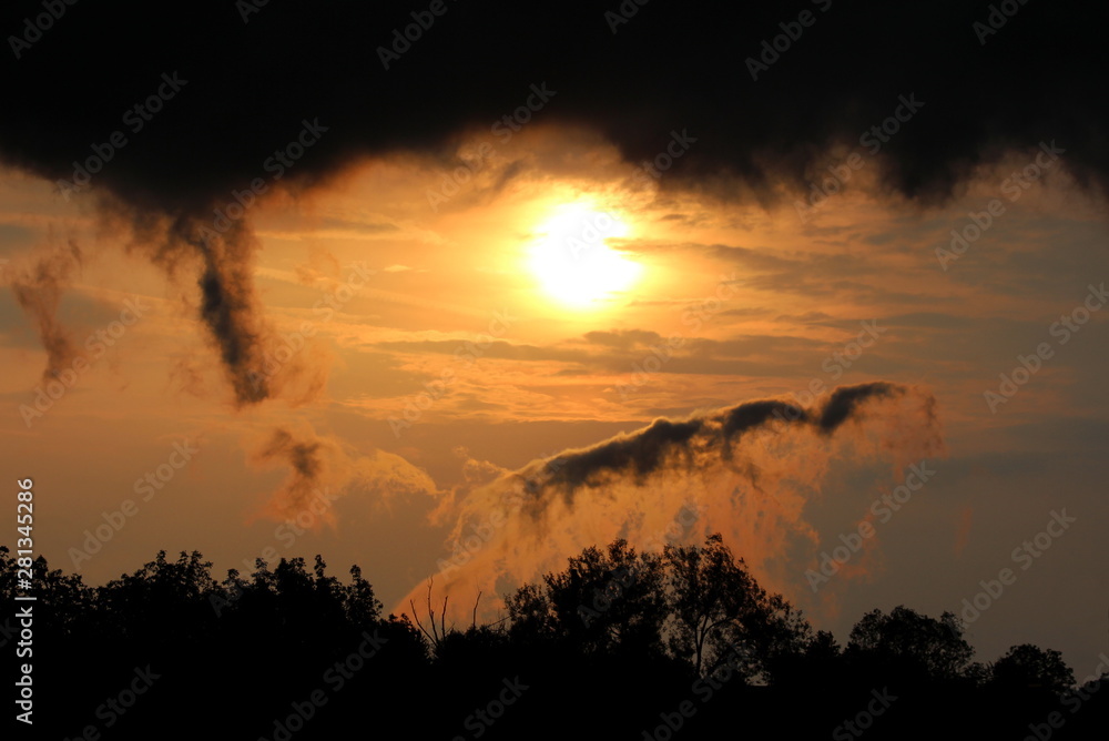 Dramatic stormy clouds surrounding sun at sunset over local forest on warm sunny spring day