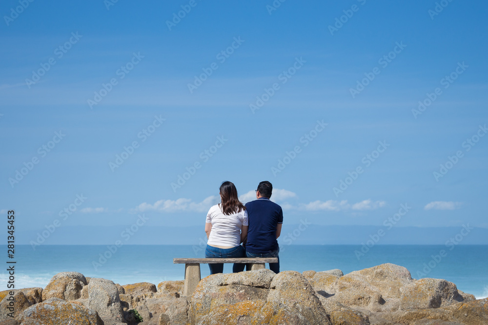Fototapeta premium Couple sitting on a bench watching the ocean