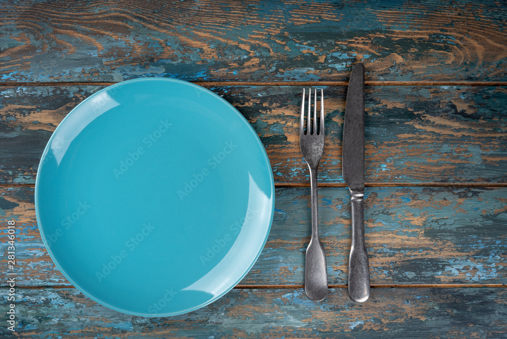 Empty plate with fork and knife on colored wooden background, top view, copy space, mock-up