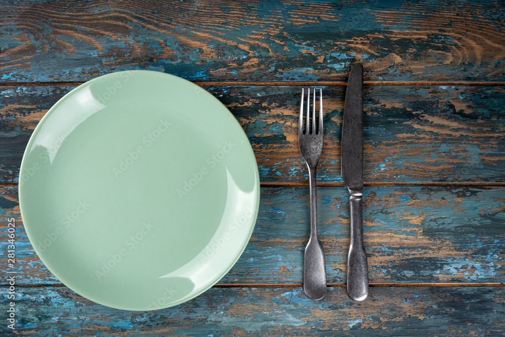 Empty plate with fork and knife on colored wooden background, top view, copy space, mock-up