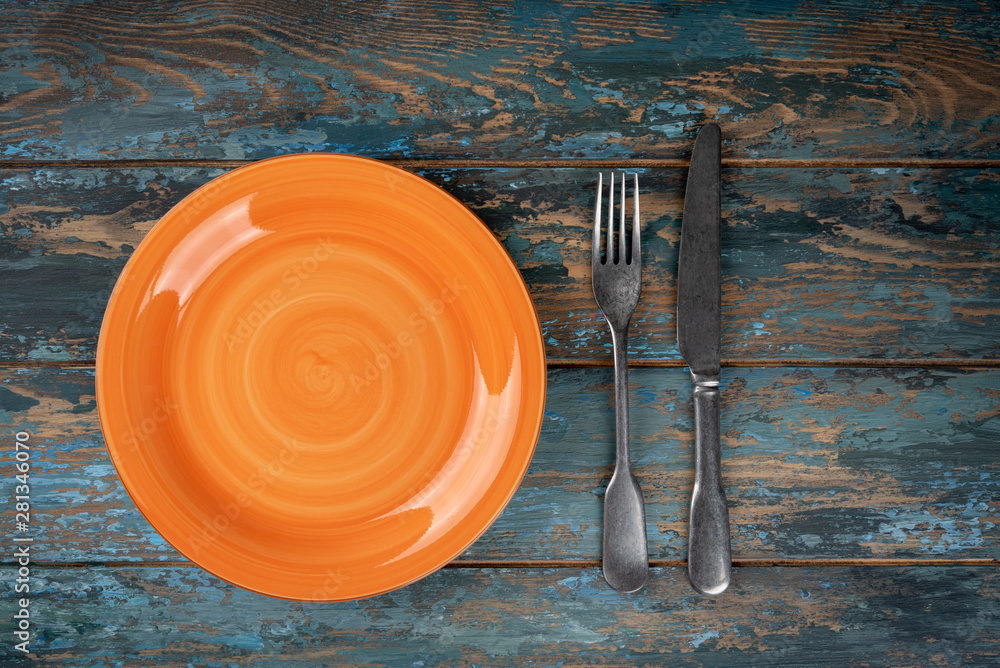 Empty plate with fork and knife on colored wooden background, top view, copy space, mock-up
