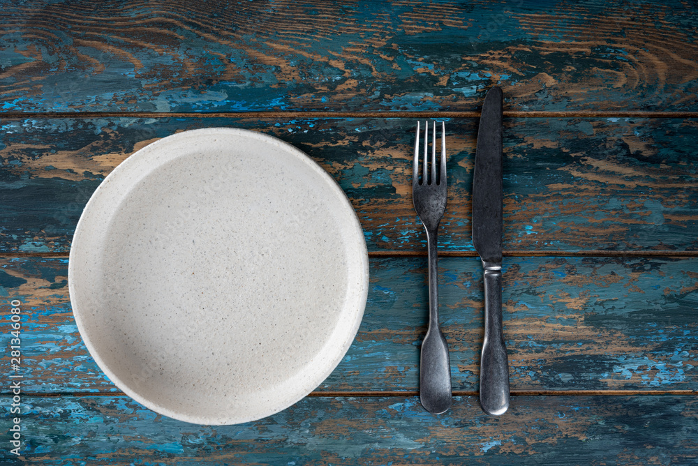 Empty plate with fork and knife on colored wooden background, top view, copy space, mock-up