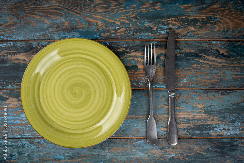Empty plate with fork and knife on colored wooden background, top view, copy space, mock-up