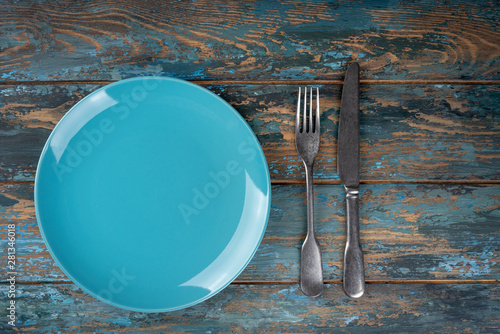 Obraz na płótnie Empty plate with fork and knife on colored wooden background, top view, copy space, mock-up w salonie