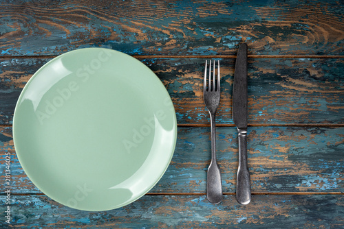 Empty plate with fork and knife on colored wooden background, top view, copy space, mock-up