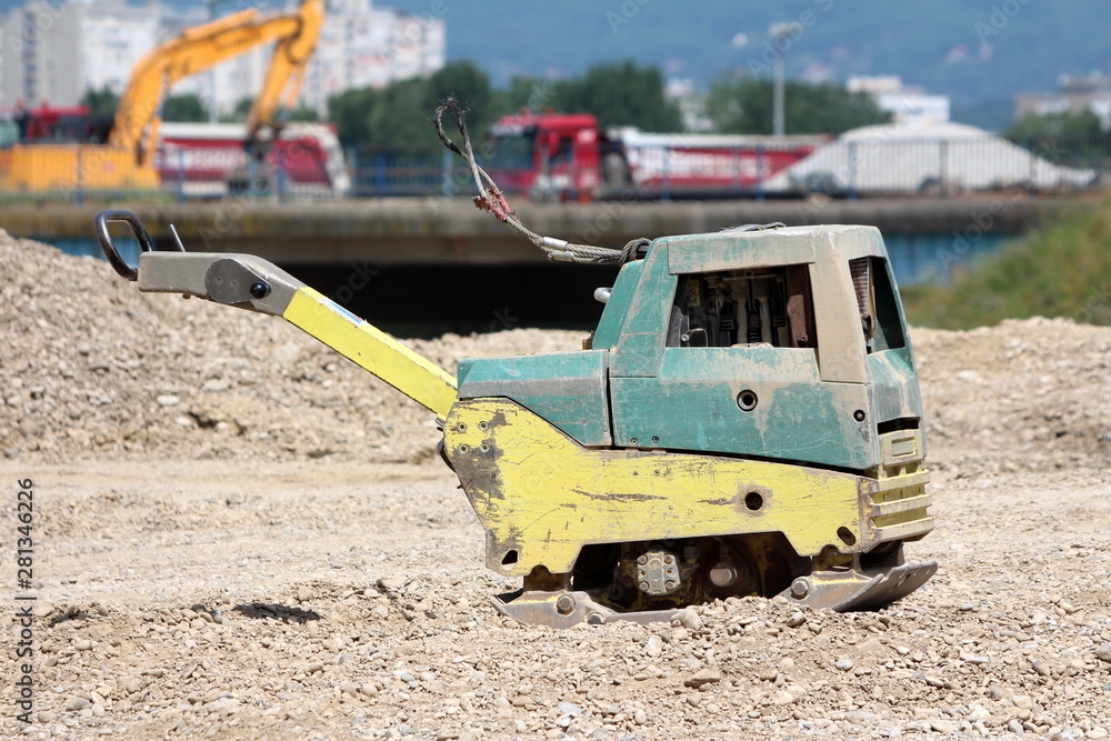 Heavily used dilapidated construction equipment vibratory plate at local construction site surrounded with gravel and sand on warm sunny spring day