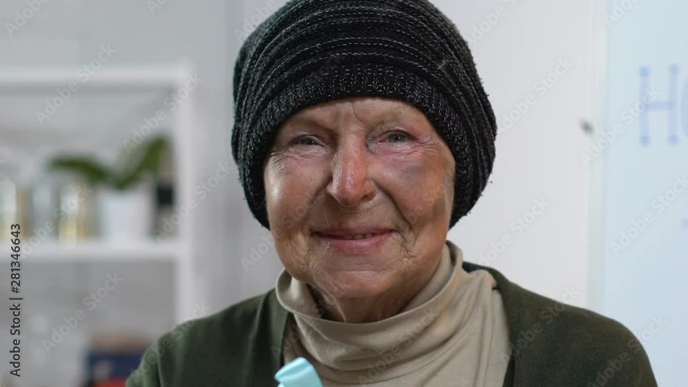 Smiling homeless woman holding gift box and looking to camera, pleasant surprise Smiling homeless woman holding gift box and looking to camera, pleasant surprise