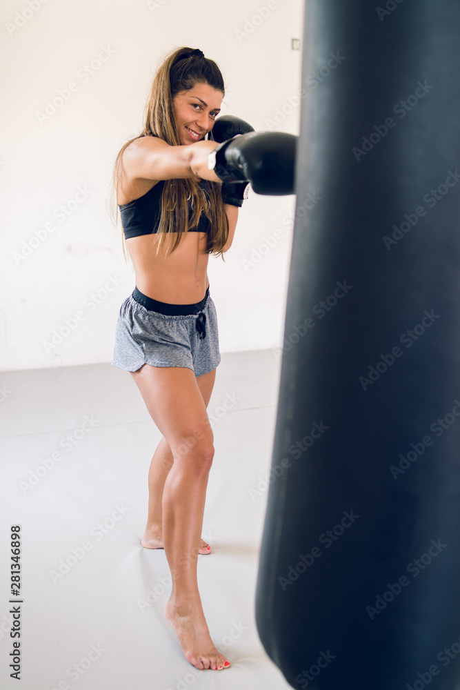 Young woman training boxing punching heavy bag with gloves on her hands at the gym martial arts academy