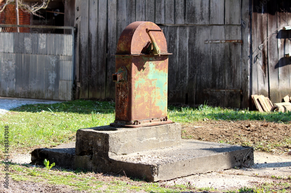 Large vintage retro partially rusted public hand water pump mounted on  dilapidated concrete foundation surrounded with grass and wooden barn in  background on warm sunny spring day Stock Photo | Adobe Stock