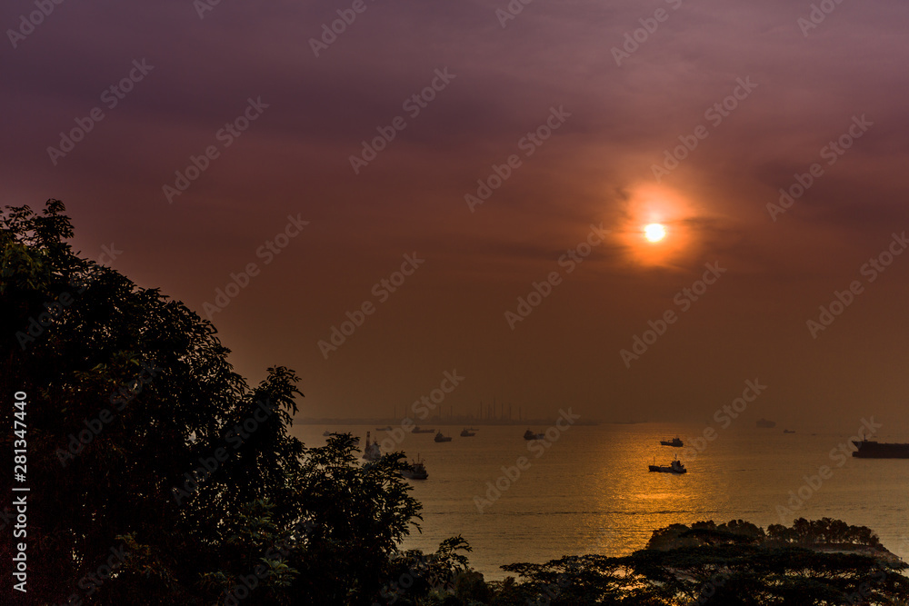 View looking out over the Singapore Strait during sunset with boats, vessels and cargo ships importing and exporting goods on the horizon