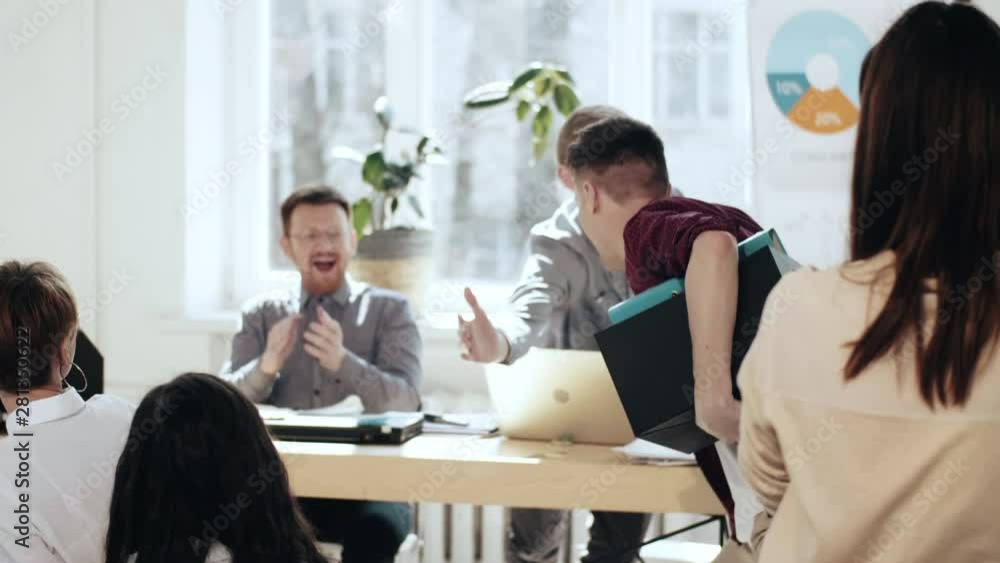 Happy young man with box walks along multiethnic office giving high fives to colleagues after career success achievement Happy young man with box walks along multiethnic office giving high fives to colleagues after career success achievement