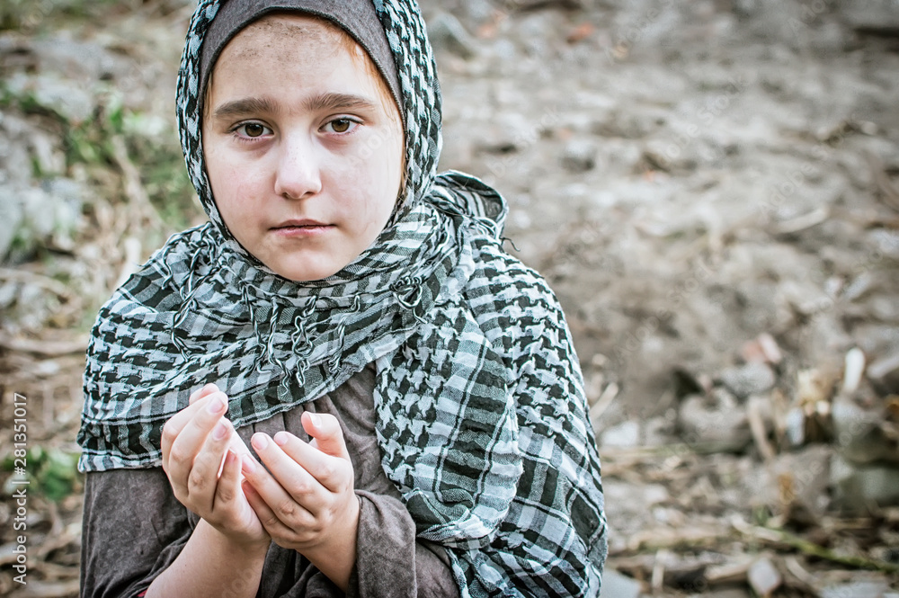 Fototapeta premium a refugee child in the war, a Muslim girl with a dirty face on the ruins, the concept of peace and war, the child is crying and waiting for help.