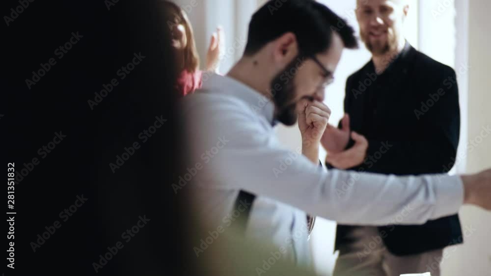 Happy young Caucasian male boss walks along modern light office giving high fives to partners after career achievement. Happy young Caucasian male boss walks along modern light office giving high fives to partners after career achievement.