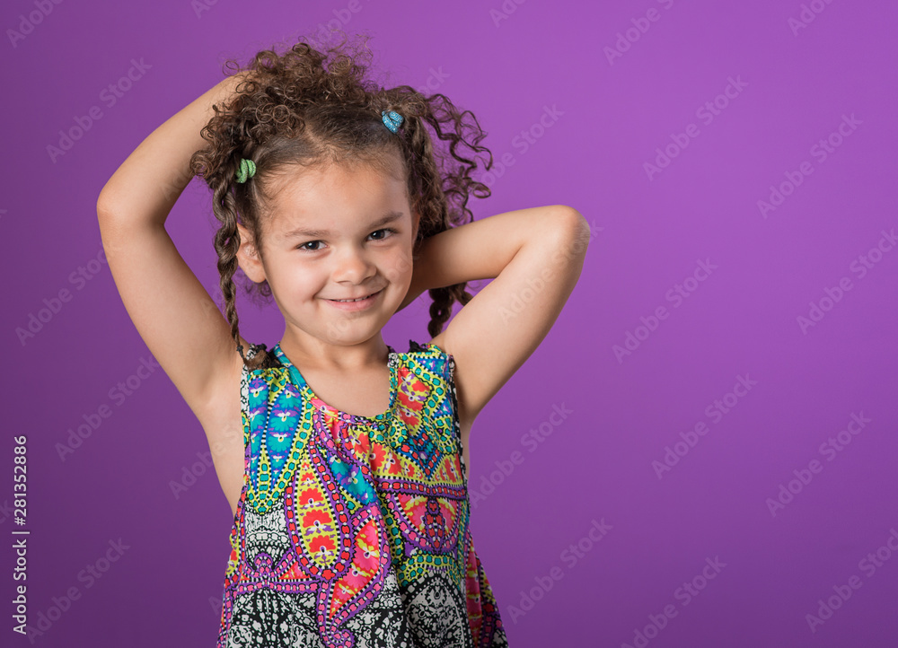 Mixed race little girl arms raised to her curly brown hair isolated on purple background Mixed race little girl arms raised to her curly brown hair isolated on purple background