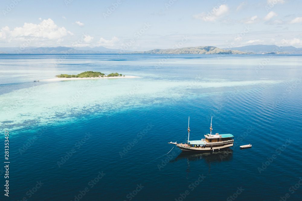 Luxury cruise boat sailing near coral reef atoll island with amazing white tropical beach and mountains on horizon. Aerial view. Luxury marine travel and vacations concept.