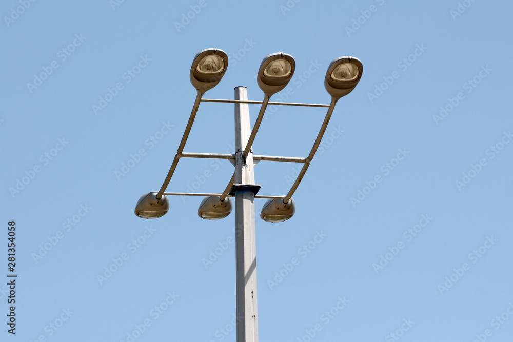 Tall strong metal utility pole with six large modern light reflectors mounted on top on clear blue sky background Tall strong metal utility pole with six large modern light reflectors mounted on top on clear blue sky background