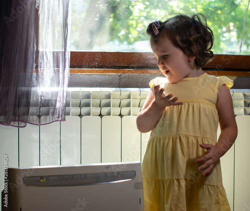 Little girl in a dusty room. Air purifier and coughing kid. Dust in the air. photo