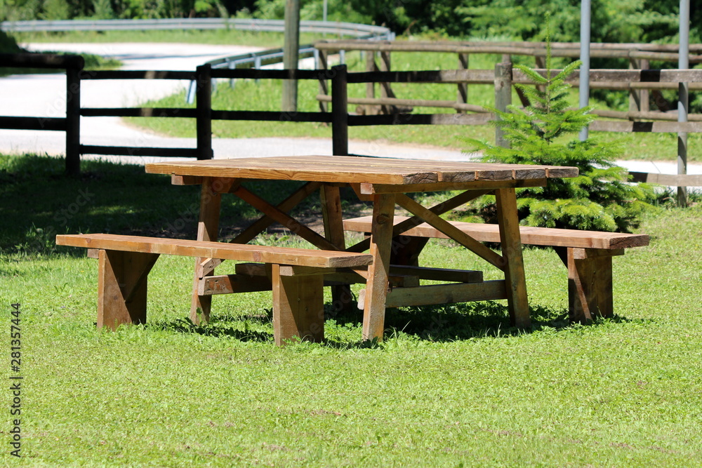 Wooden table with two benches in family house backyard surrounded with green grass next to paved road on warm sunny spring day Wooden table with two benches in family house backyard surrounded with green grass next to paved road on warm sunny spring day