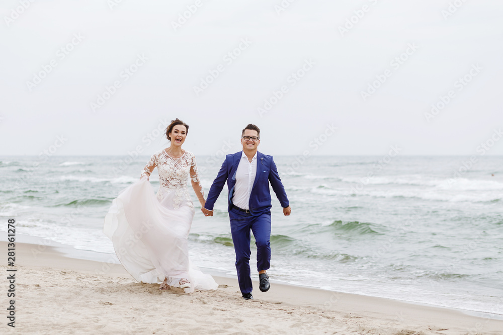 newlyweds run along the beach along the sea in cloudy weather newlyweds run along the beach along the sea in cloudy weather