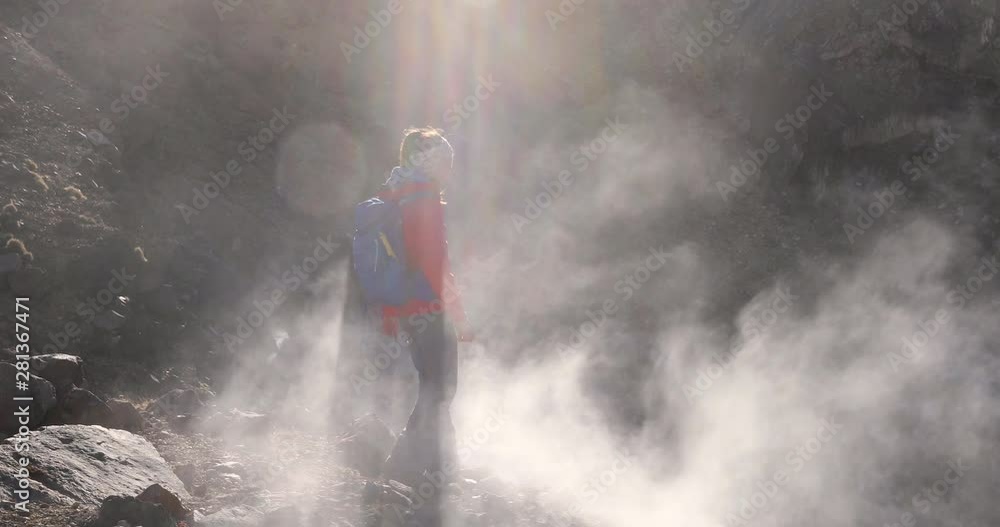 Woman hiking on active volcano with smoke and fumes, tramping track at Tongariro National Park in New Zealand. Woman backpacker on hike walking in mountains. 59.94 FPS slow motion. Woman hiking on active volcano with smoke and fumes, tramping track at Tongariro National Park in New Zealand. Woman backpacker on hike walking in mountains. 59.94 FPS slow motion.