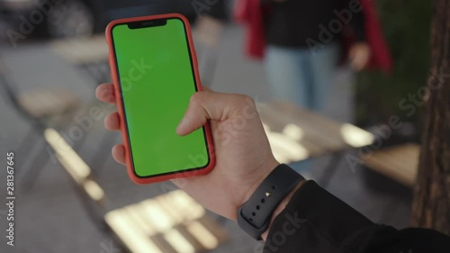 Busy young man holding using a modern smartphone with green chromekey screen for copy space outdoors in the city. People life and technology. photo