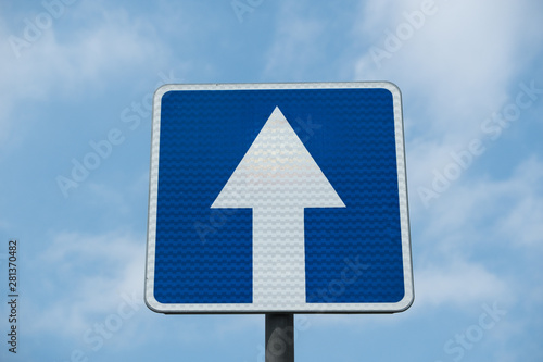 Road sign against the sky. Blue sign "Go straight" White arrow, on a blue background. Summer day.