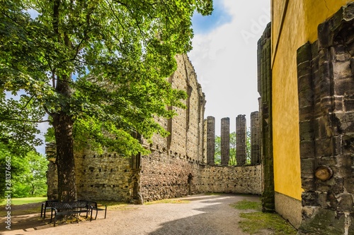 Panensky Tynec, Czech Republic - July 15 2019: Stone ruins of the unfinished Gothic church of the Virgin Mary from 14th century. Sunny summer day with blue sky and white clouds. Green tree with bench.