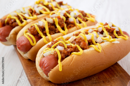 Homemade Detroit style chili dog on a rustic wooden board on a white wooden background, side view. Close-up.