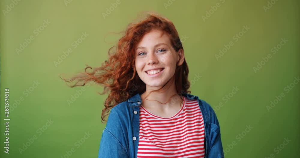 Portrait of good-looking girl with flying hair in casual clothing smiling looking at camera standing alone on green background. Beautiful young people and good mood concept. Portrait of good-looking girl with flying hair in casual clothing smiling looking at camera standing alone on green background. Beautiful young people and good mood concept.