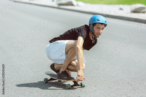 Skateboarder doing a trick at the city's street in sunny day. Young man in equipment riding and longboarding on the asphalt in action. Concept of leisure activity, sport, extreme, hobby and motion.